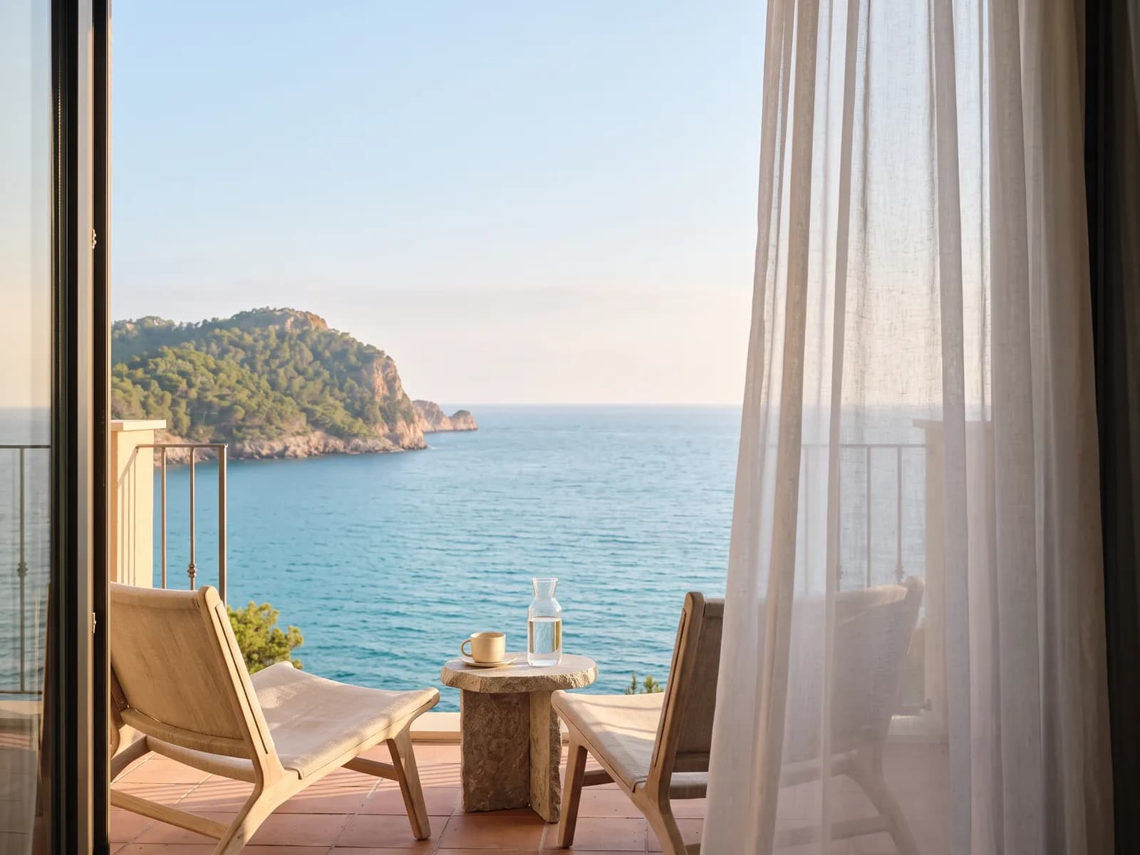 Het balkon van diezelfde hotelkamer, twee lage stoelen en een stenen tafel met uitzicht op zee